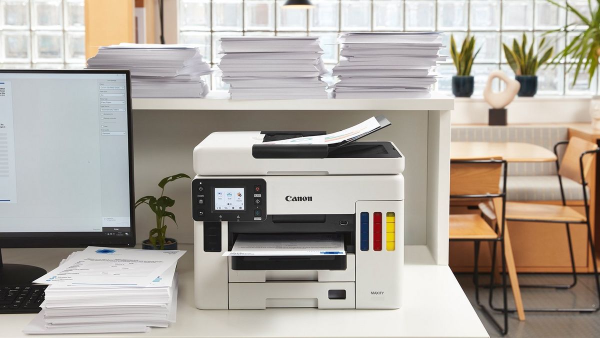 Canon kleuren printer op een bureau naast een stapel papier